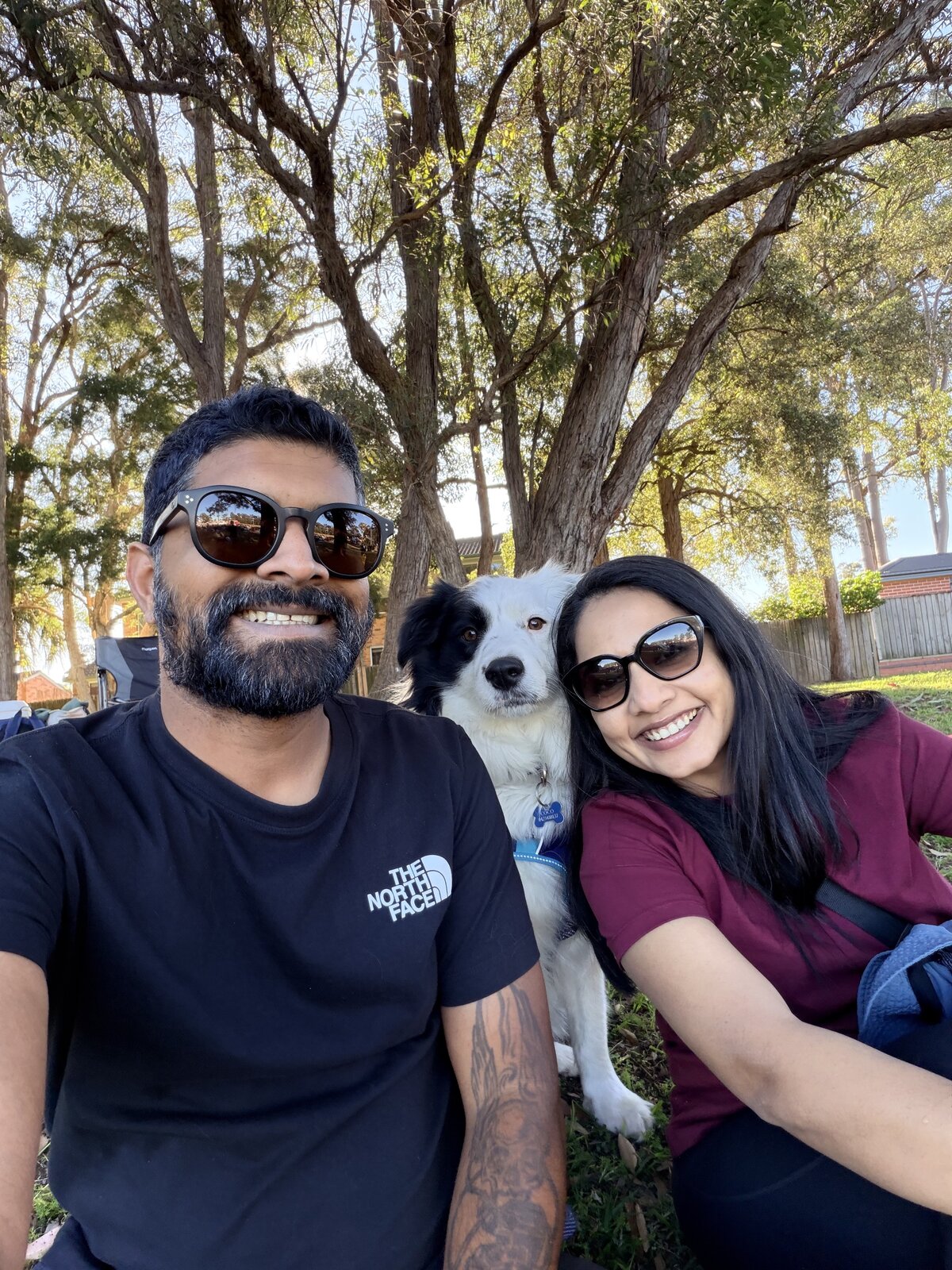 Selvin, John Peter and Coco the Border Collie smiling for a selfie under gum trees in a Sydney park